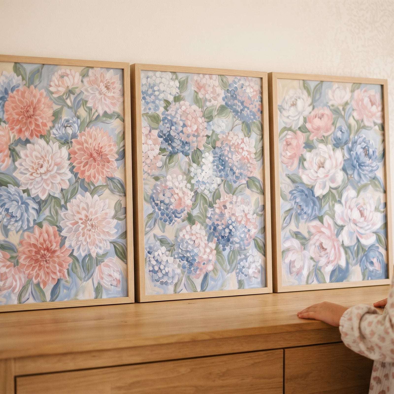 Shabby chic pastel floral wall art set of 3 on a dresser with soft pink and blue flowers next to a child's hand.