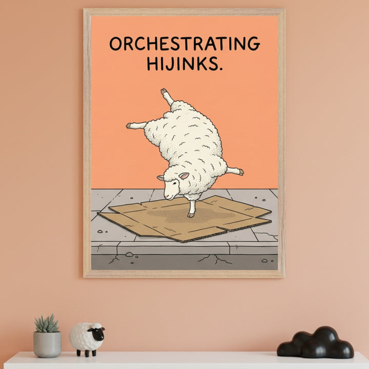 Minimalist room with a peach wall. A light wood-framed print shows a cartoon sheep balancing on one leg on cardboard, with text "ORCHESTRATING HIJINKS.". It hangs above a white shelf with a plant, sheep figurine, and black sculpture.