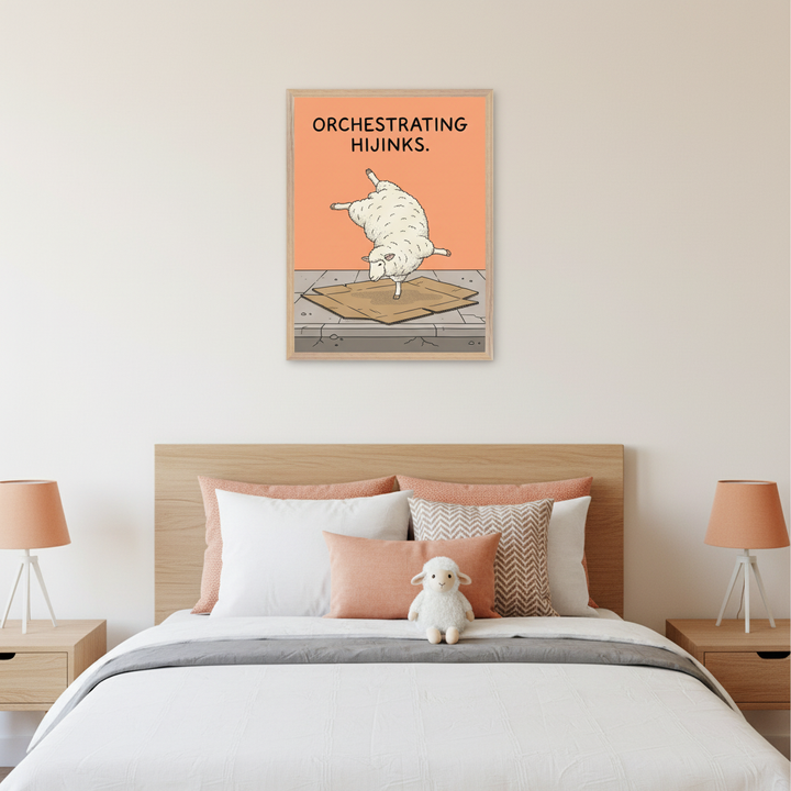 Modern bedroom with a light wood bed, headboard, and two nightstands. A framed poster hangs centrally above the bed. The poster features a cartoon white sheep doing a handstand on cardboard, with "ORCHESTRATING HIJINKS" text on an orange background.