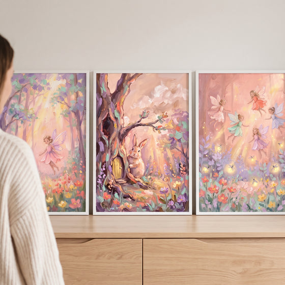 A shimmering pastel enchanted woodland wall art set of 3 with fairies and a rabbit displayed above a wooden cabinet.