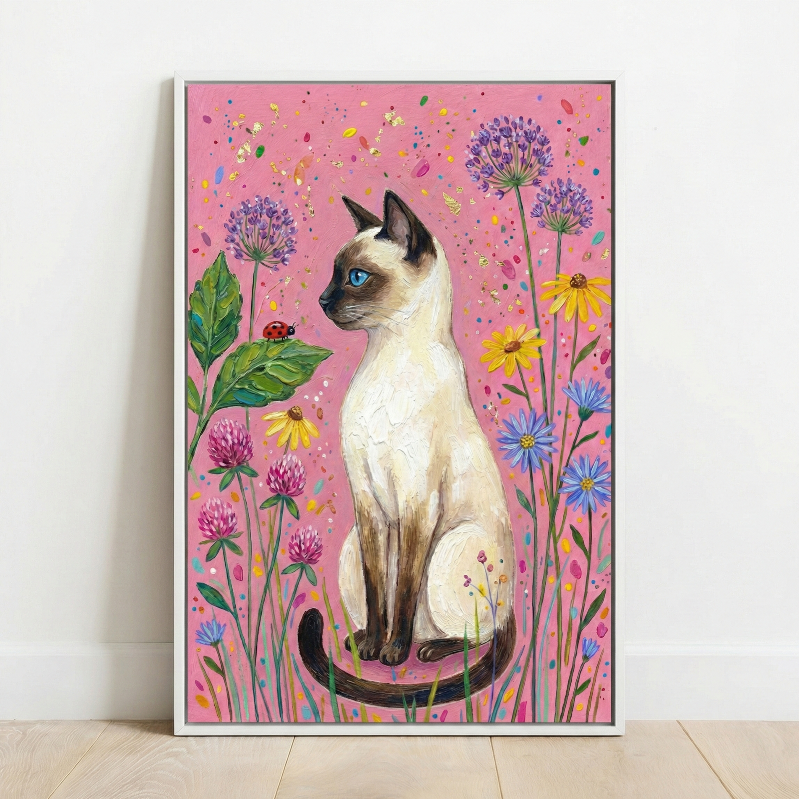 A vertical artwork of a Siamese cat with a cream body, dark points, and bright blue eyes sitting amidst colorful flowers. The cat looks toward a small ladybug on a leaf. Purple alliums, pink clovers, and yellow and blue daisies surround the feline. The background is a textured pink with multicolored specks. The scene is created with thick, visible brushstrokes. The piece is in a white frame, leaning against a white wall on a wooden floor.