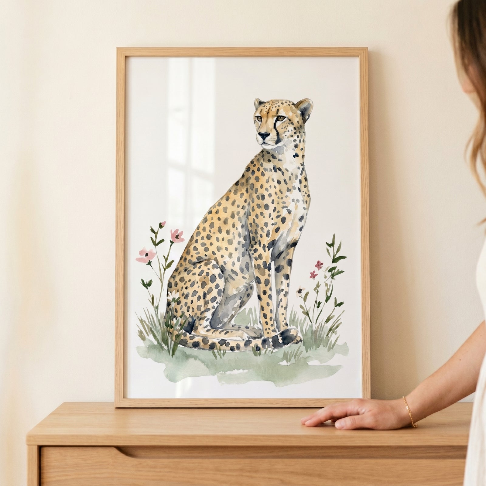 Framed sitting cheetah wall art with watercolor flowers and grass, displayed on a light wood dresser.
