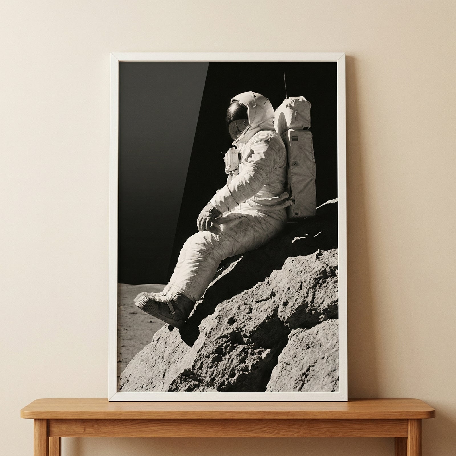 Framed monochrome sitting lunar rock astronaut wall art rests on a wooden console table against a neutral wall.