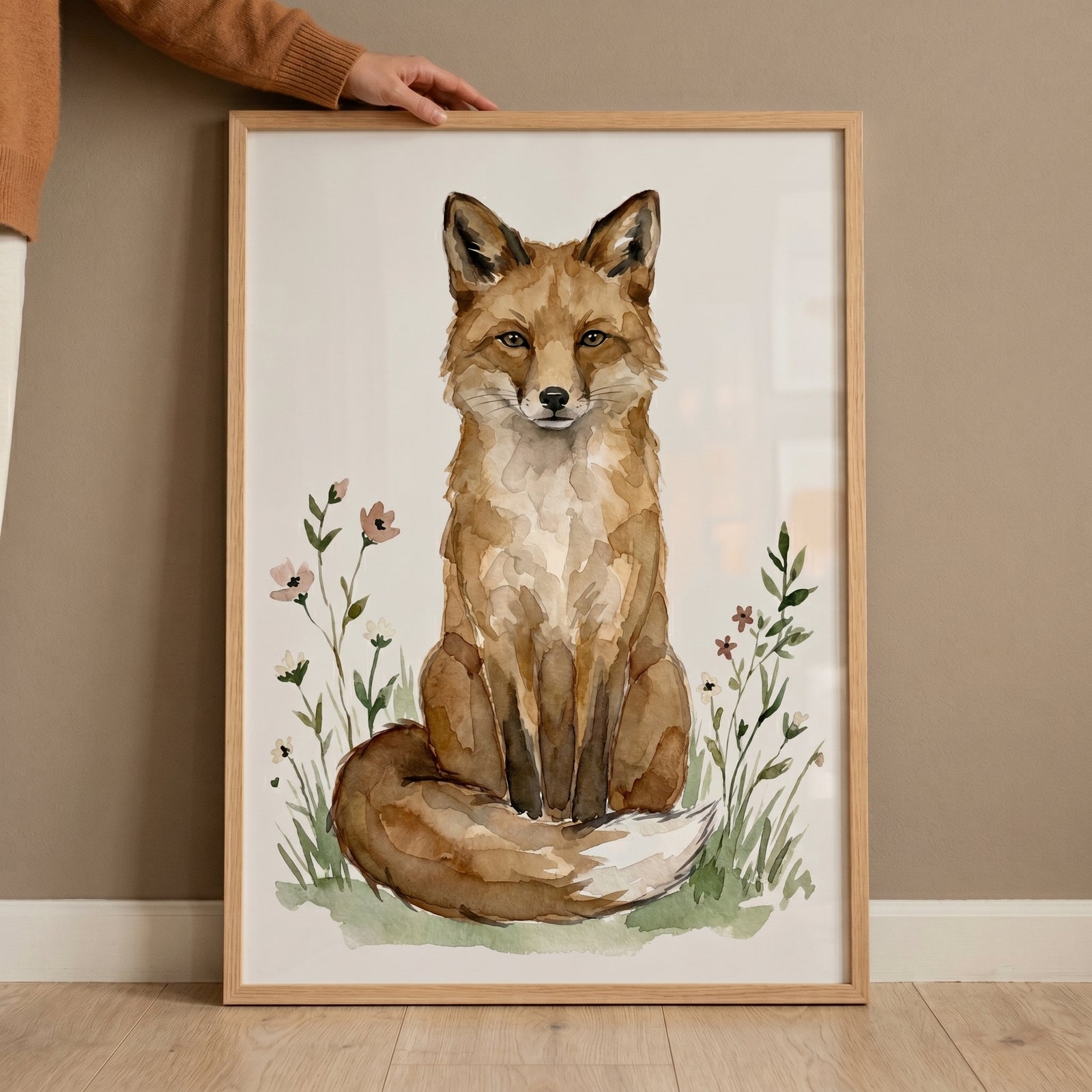 Sitting orange fox wall art in a wood frame, featuring a watercolor fox surrounded by delicate flowers and grass.