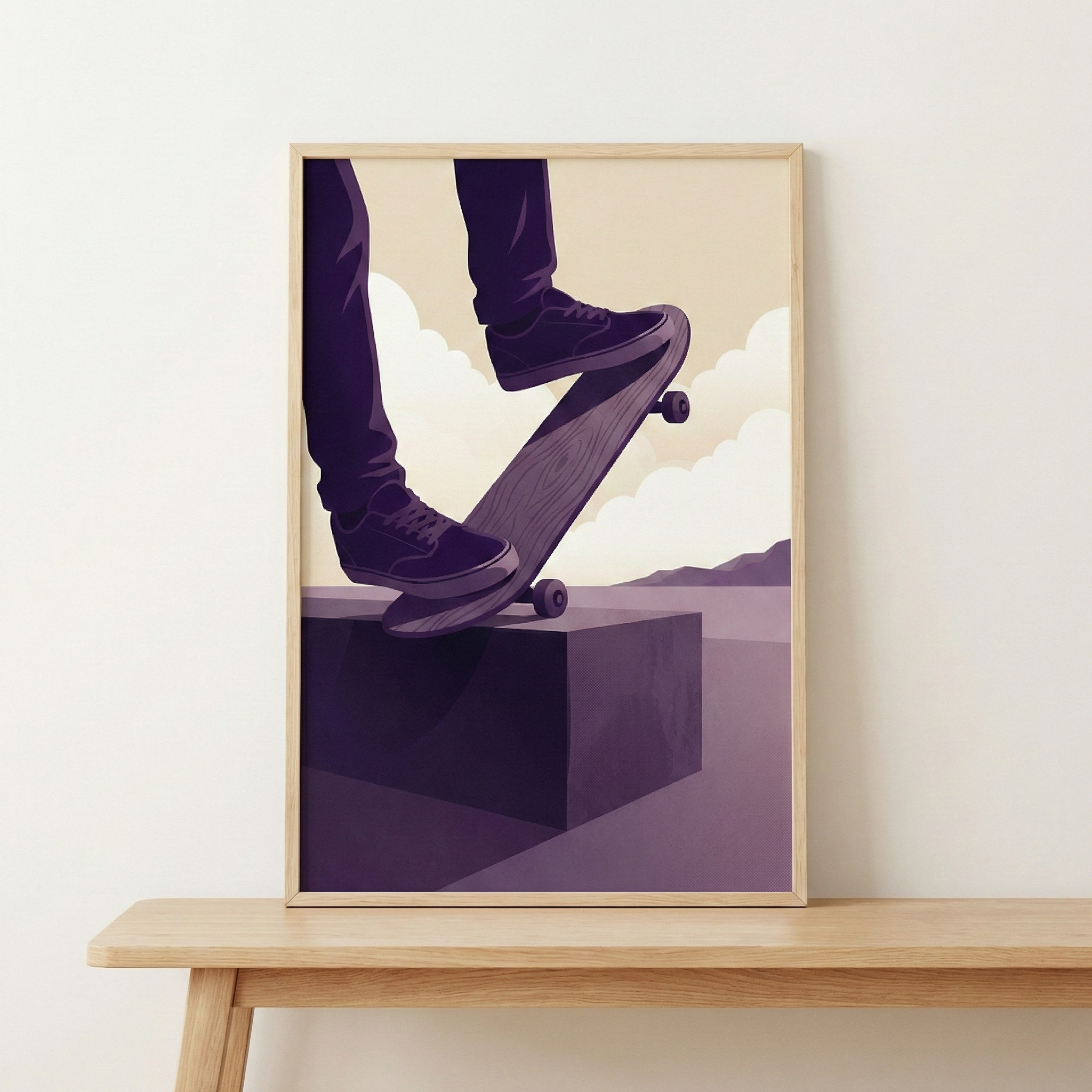 A framed graphic illustration is displayed resting on a light-colored wooden table against a plain off-white wall. The artwork depicts the lower half of a person in the middle of a skateboarding move. The person is wearing dark purple pants and matching sneakers. One foot is positioned on the tail of the skateboard, which rests on the edge of a solid, dark purple rectangular block. 