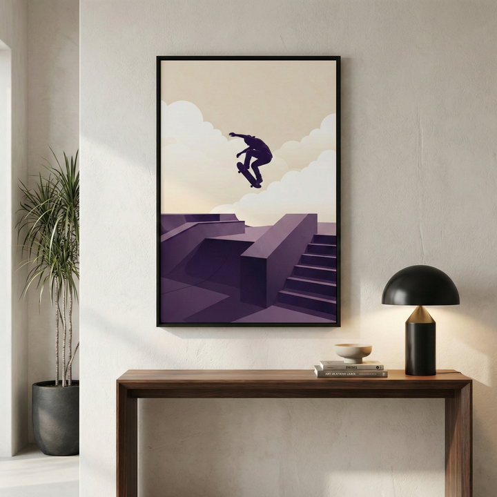 A minimalist artwork in a sleek black frame, hanging on a textured neutral wall. The art depicts a dark silhouette of a skateboarder mid-air, performing a trick above a stylized skatepark composed of geometric shapes, ramps, and stairs in shades of deep purple. The background features a layered sky of beige and cream with soft, rounded white clouds. Below the frame sits a mid-century modern wooden console table. 