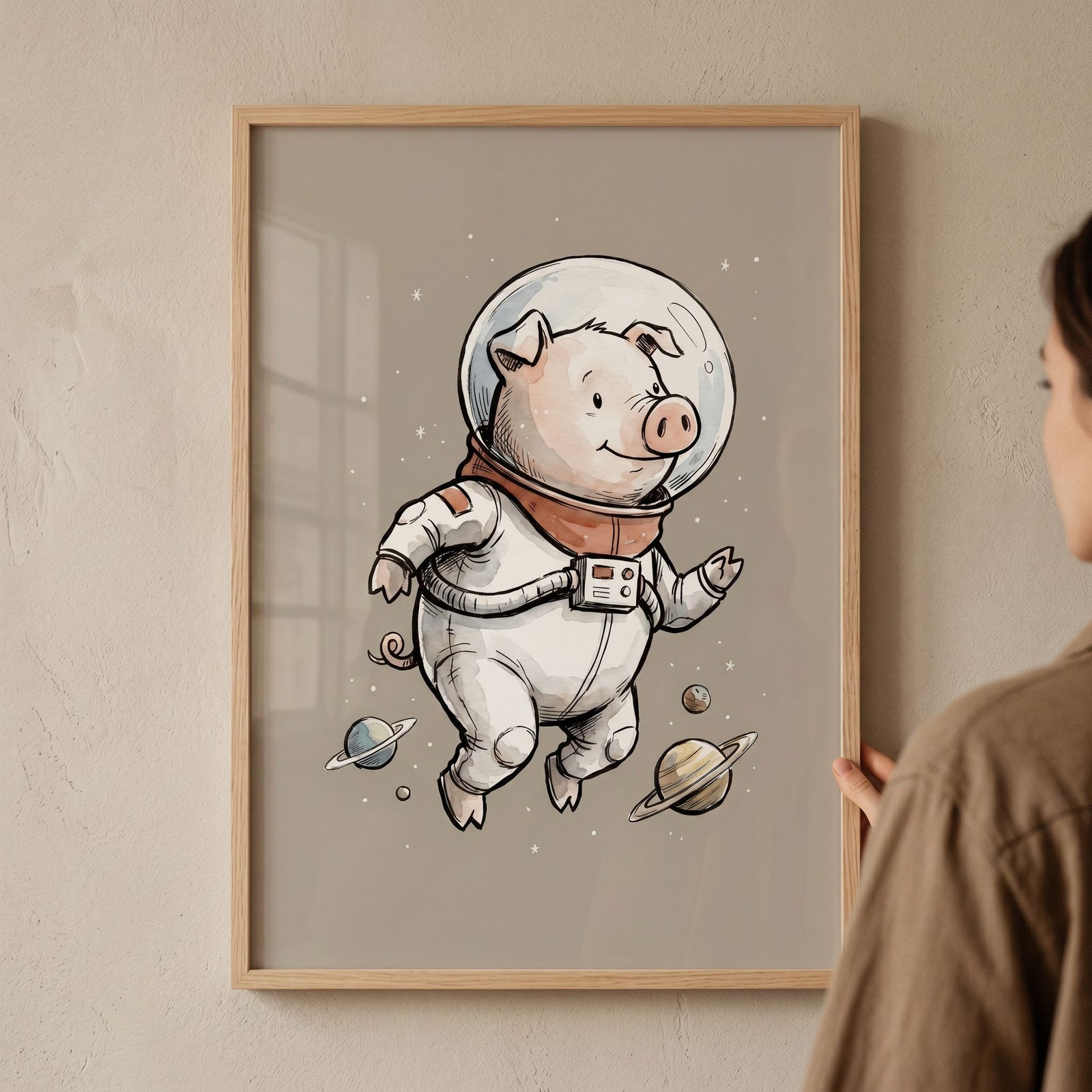 A person holds framed sketch style space pig wall art of a cute pig in an astronaut suit floating past planets.