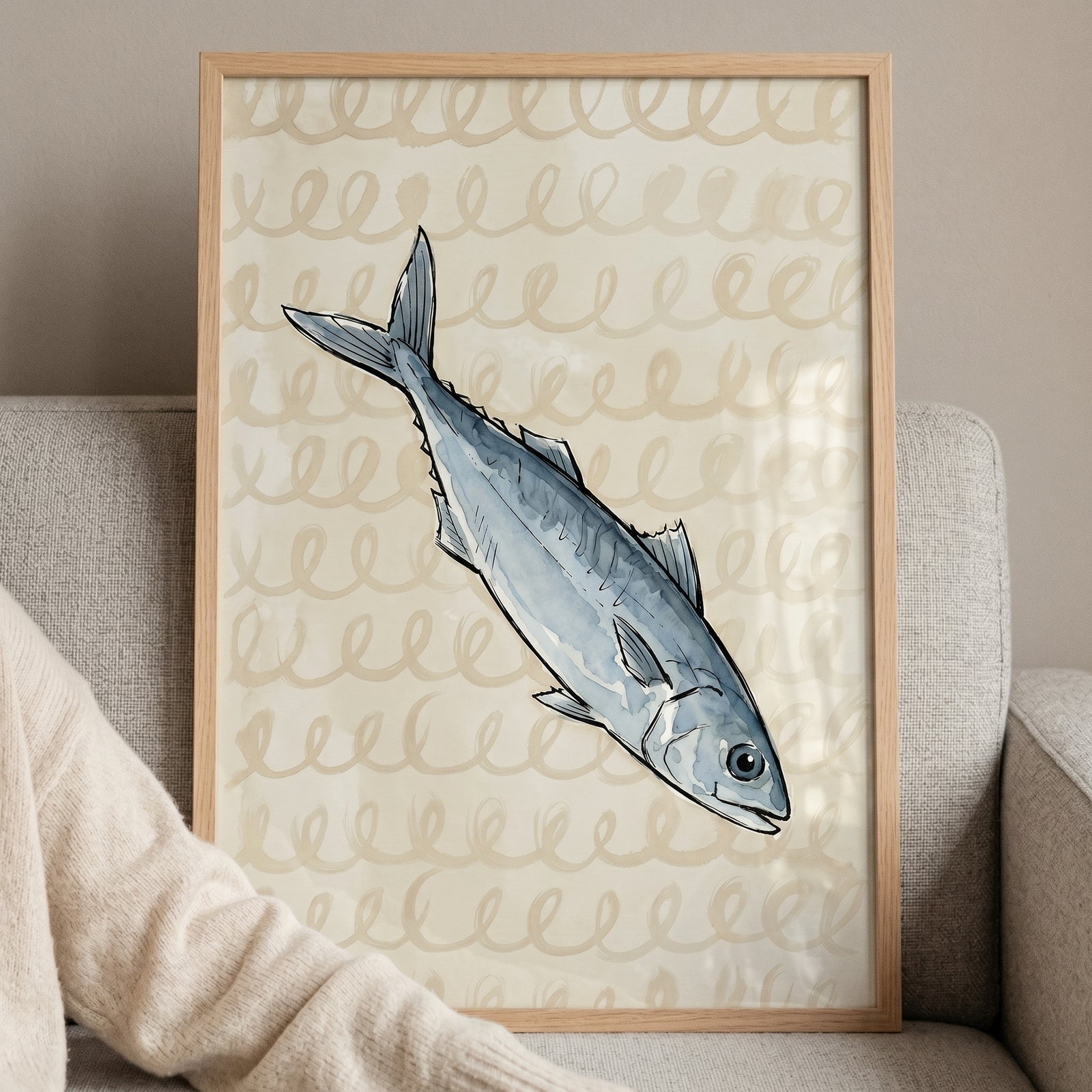 Sketchy silver blue mackerel fish wall art in a light wood frame on a grey couch with a swirling beige background.