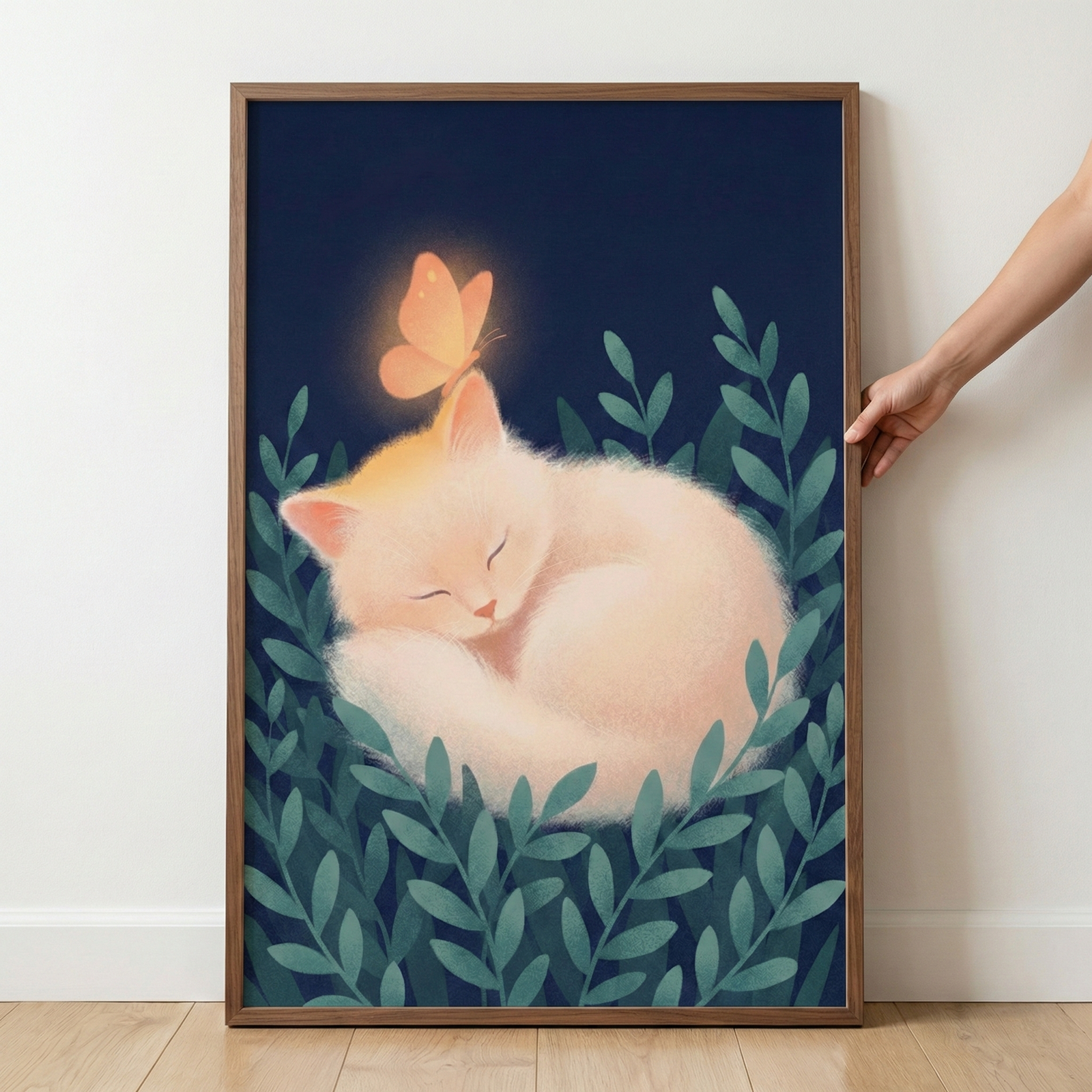 A vertical digital illustration presented in a thin wooden frame. At its center, a soft, fluffy cream-colored cat is curled into a peaceful sleep. A glowing orange butterfly rests gently on the cat’s head, radiating a warm light. The animal is nestled among stylized dark green leaves against a deep navy blue background. The overall style is whimsical and serene, with a soft, textured finish. A person’s hand is visible on the right, holding the frame against a plain white wall.