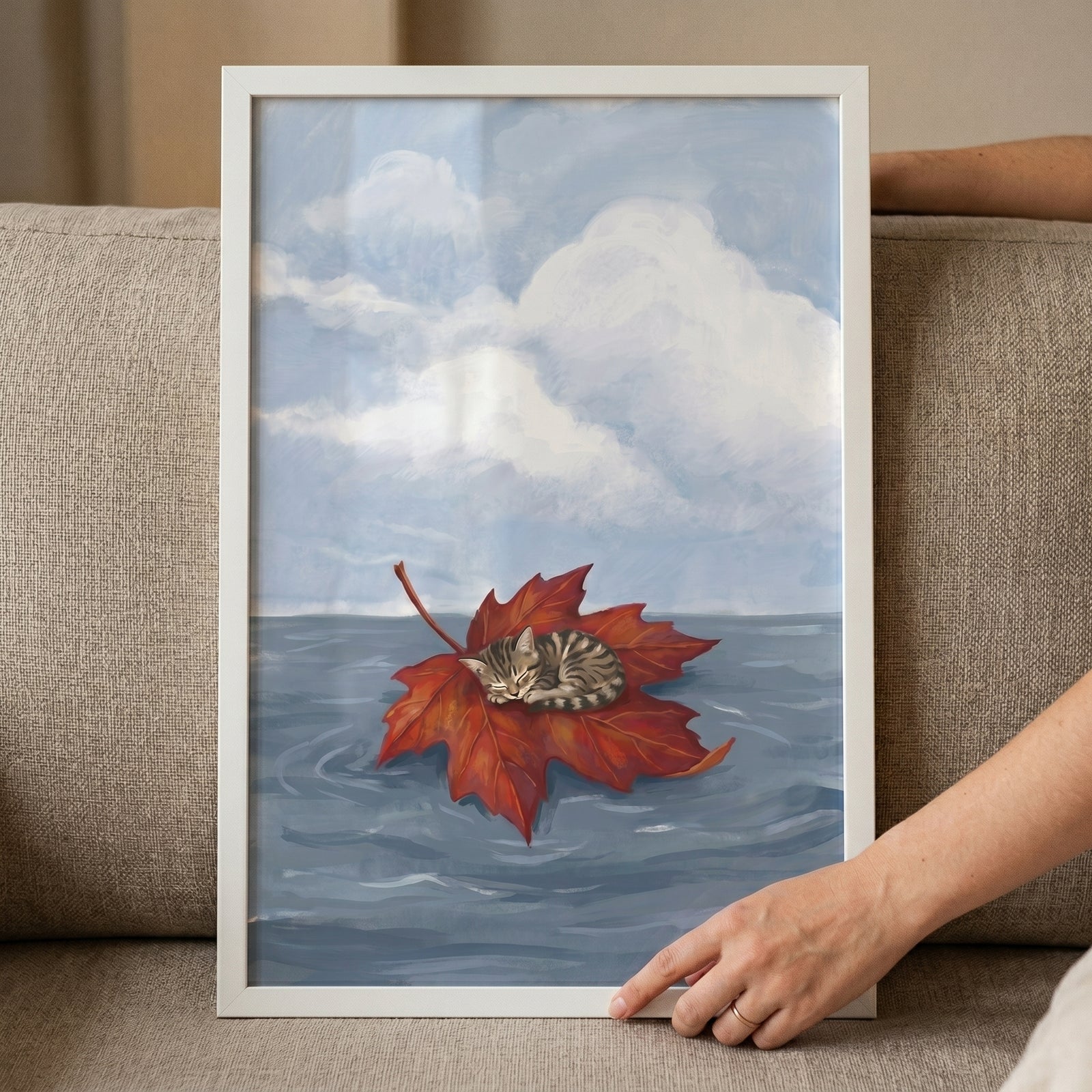 Framed sleeping maple leaf kitten wall art shows a tabby cat resting on a red leaf floating on water.