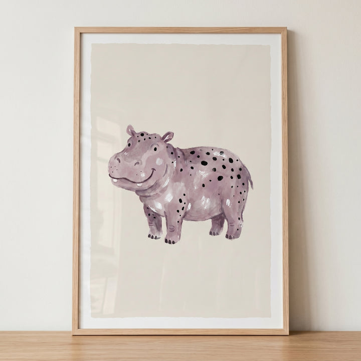 A smiling black spotted hippo artwork in purple watercolor, set in a light wood frame on a wooden surface.