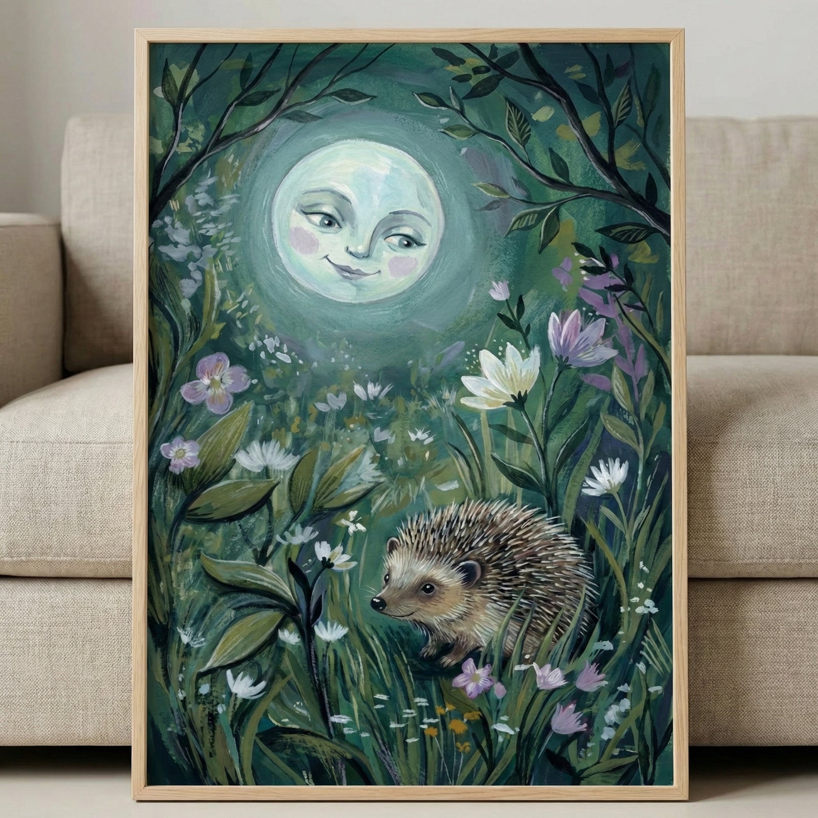A vertical, framed artwork featuring a whimsical night scene. A large, glowing moon with a gentle, smiling human face occupies the upper center. Below, a small, detailed hedgehog walks through a lush meadow of tall grass, white daisies, and purple flowers. Dark, leafy branches frame the top edges. The piece has visible, textured brushwork in deep greens, teals, and soft highlights. The light wood frame rests against a neutral-toned fabric sofa.
