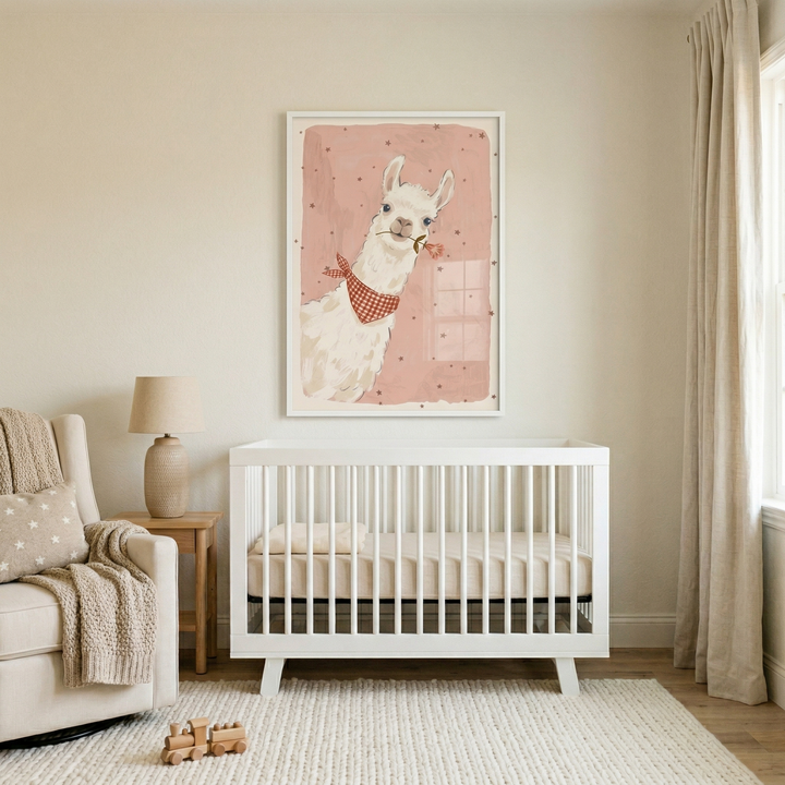 A softly lit, contemporary nursery features a neutral color palette. Centered on a beige wall is a large, white-framed illustration of a white cartoon llama. The llama has a friendly expression, wears a red and white checkered neckerchief, and holds a small pink flower in its mouth, set against a muted pink background with scattered darker dots. 