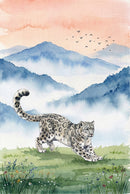 A watercolor-style illustration of a snow leopard with a thick, spotted coat stretching its front legs on a green, grassy meadow. The foreground is dotted with small, delicate wildflowers in shades of blue, white, and yellow. In the background, layers of blue mountains are partially obscured by soft, ethereal mist. The sky above is a pale peach and orange gradient, with a small flock of birds flying across the upper right. The entire scene has a soft, textured finish.