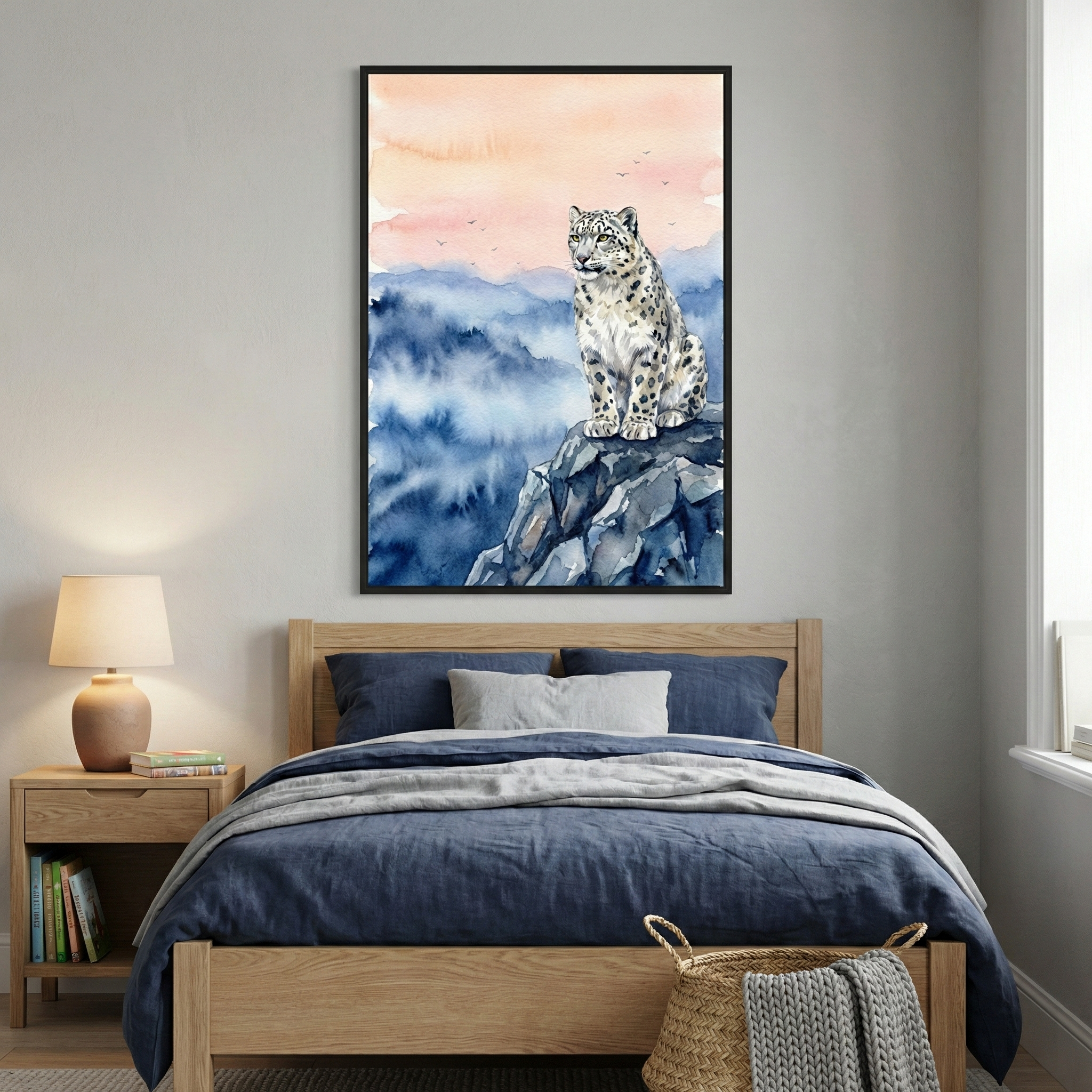 A cozy bedroom features a wooden bed with blue bedding and a white pillow. On the wall above the bed hangs a framed watercolor painting of a snow leopard perched on a rocky cliff against a backdrop of pink and blue sky. A wooden nightstand with a lamp and books completes the serene setting.