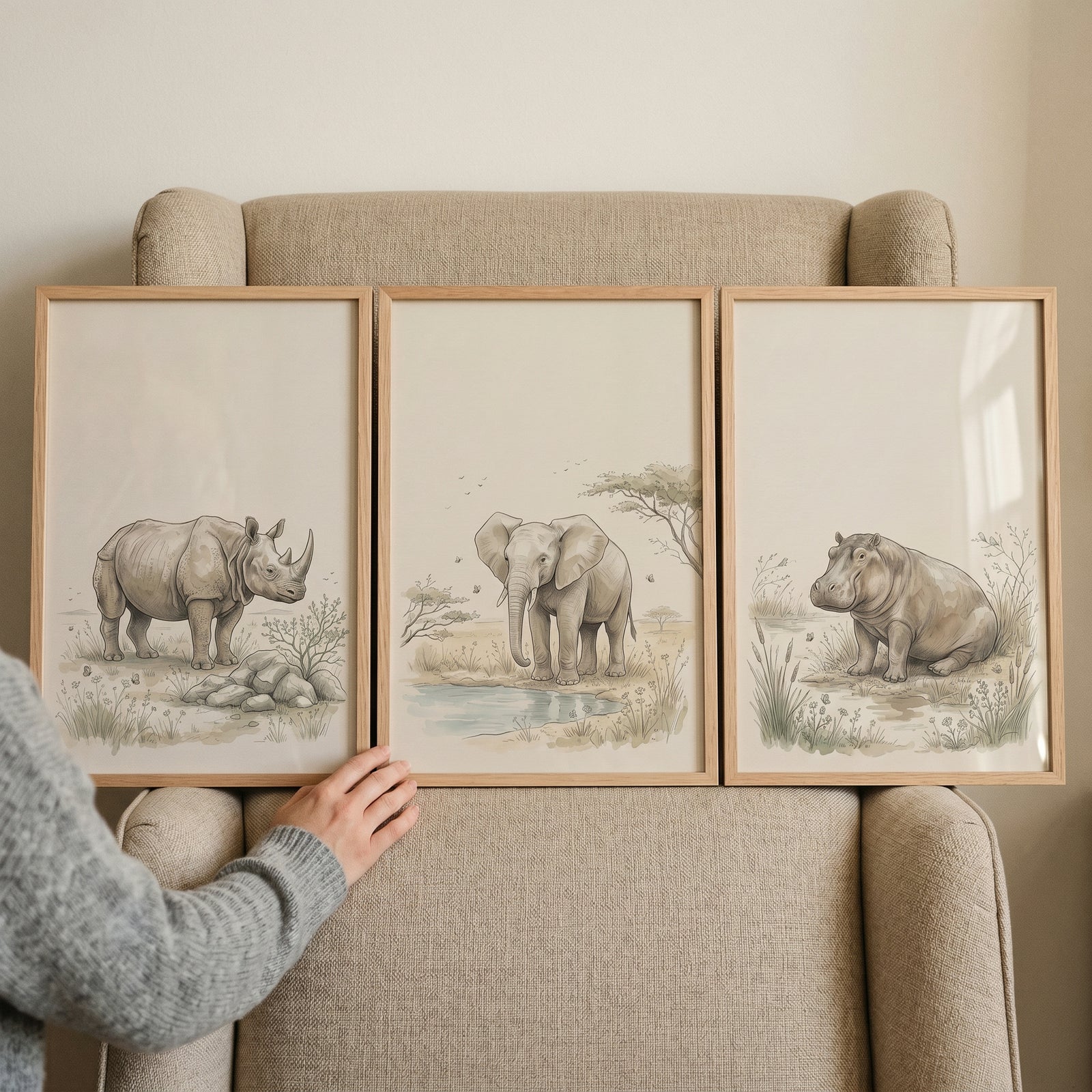 Framed soft beige savanna animal wall art set of 3 with a rhino, elephant, and hippo on a neutral armchair.
