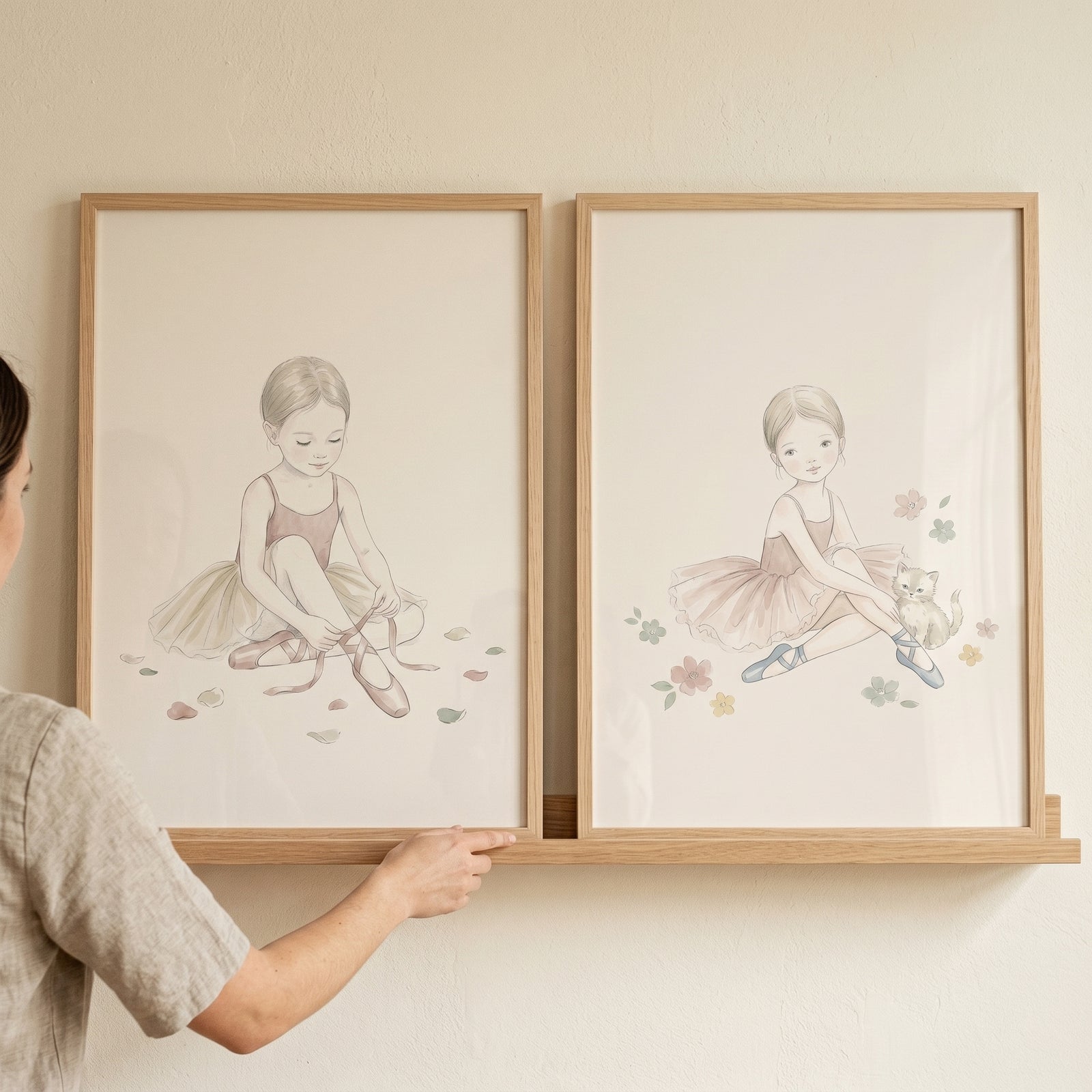 Hand adjusts a soft beige sitting ballerina wall art set of 2 featuring dancers and a cat in wood frames on a shelf.