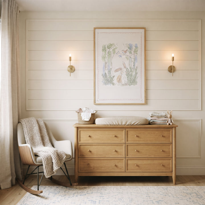 Soft birch tree bunny wall art above a wood dresser in a neutral nursery with a rocking chair and knit throw.