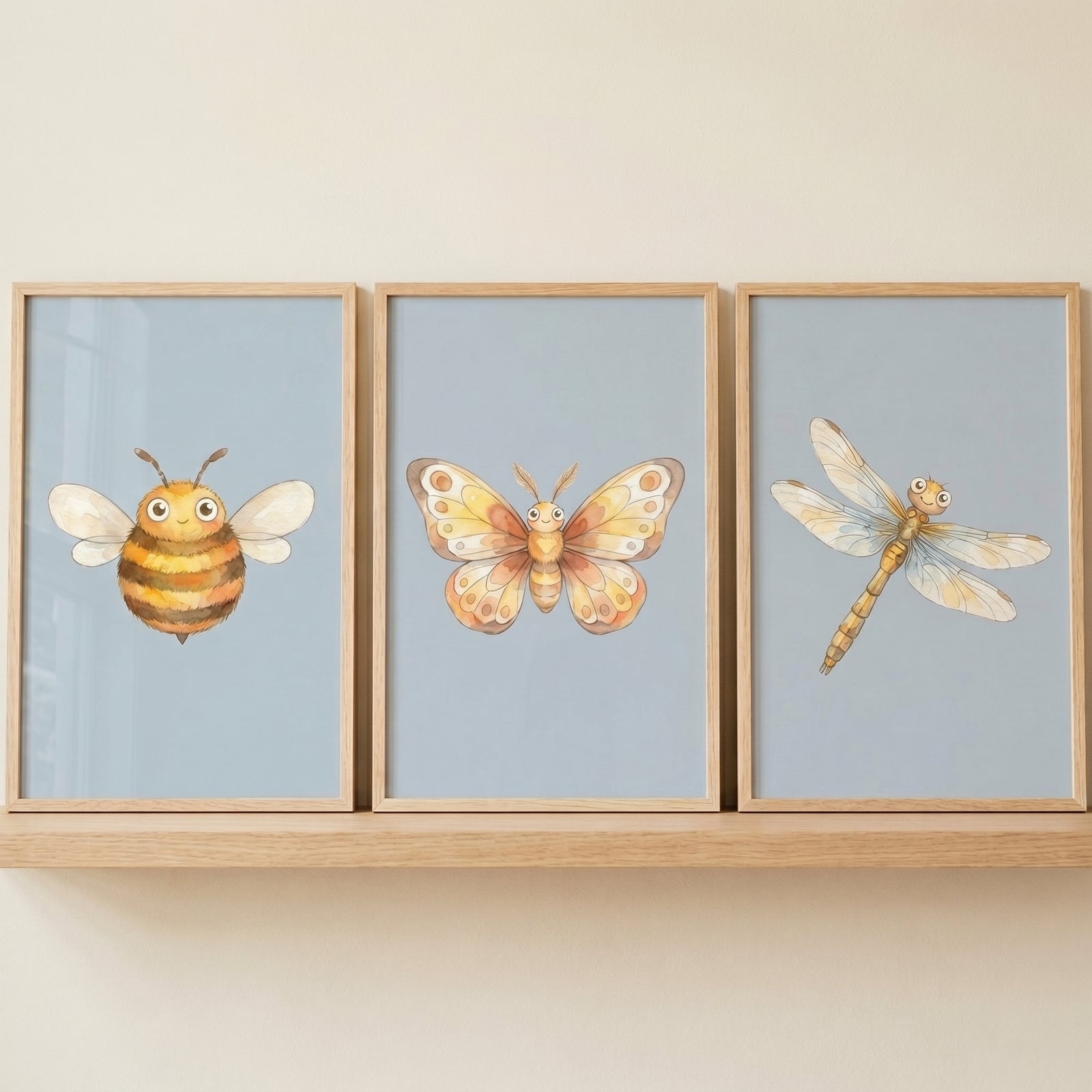 Watercolor bee, butterfly, and dragonfly in a soft blue insect wall art set of 3 displayed in light wood frames.
