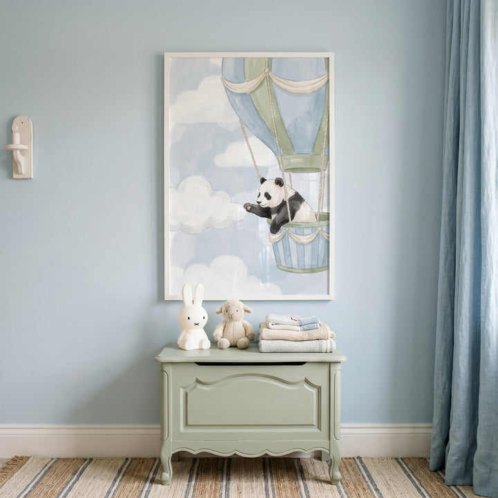 Soft blue sky panda artwork above a sage chest with a rabbit lamp and plush lamb. Light blue walls and blue curtains.