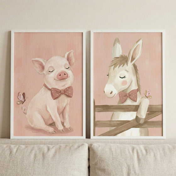 Two vertical white-framed art prints hang side-by-side on a light beige wall above a neutral-toned fabric sofa. 

The print on the left features a whimsical, soft pink pig with closed eyes and a contented expression. The pig is sitting and wearing a dark pink bow tie decorated with white polka dots. A small butterfly with pink and brown wings is shown fluttering near the pig's ear.
