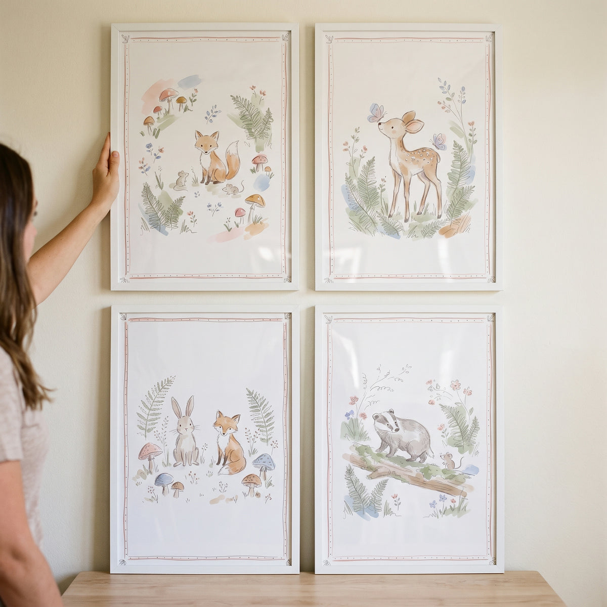 Person hangs a soft fern woodland animal wall art set of 4 featuring a fox, deer, rabbit, and badger in white frames.
