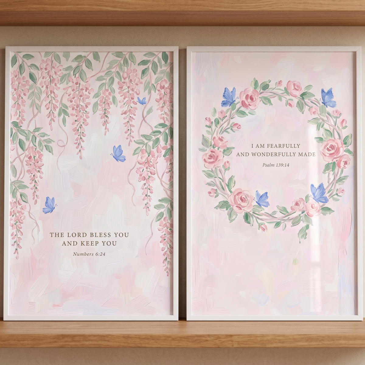 Soft floral bible verse wall art set of 2 with pink flowers and blue butterflies in white frames on a wooden shelf.