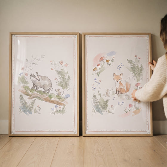 A soft garden woodland animal wall art set of 2 with watercolor illustrations of a fox and badger in light wood frames.