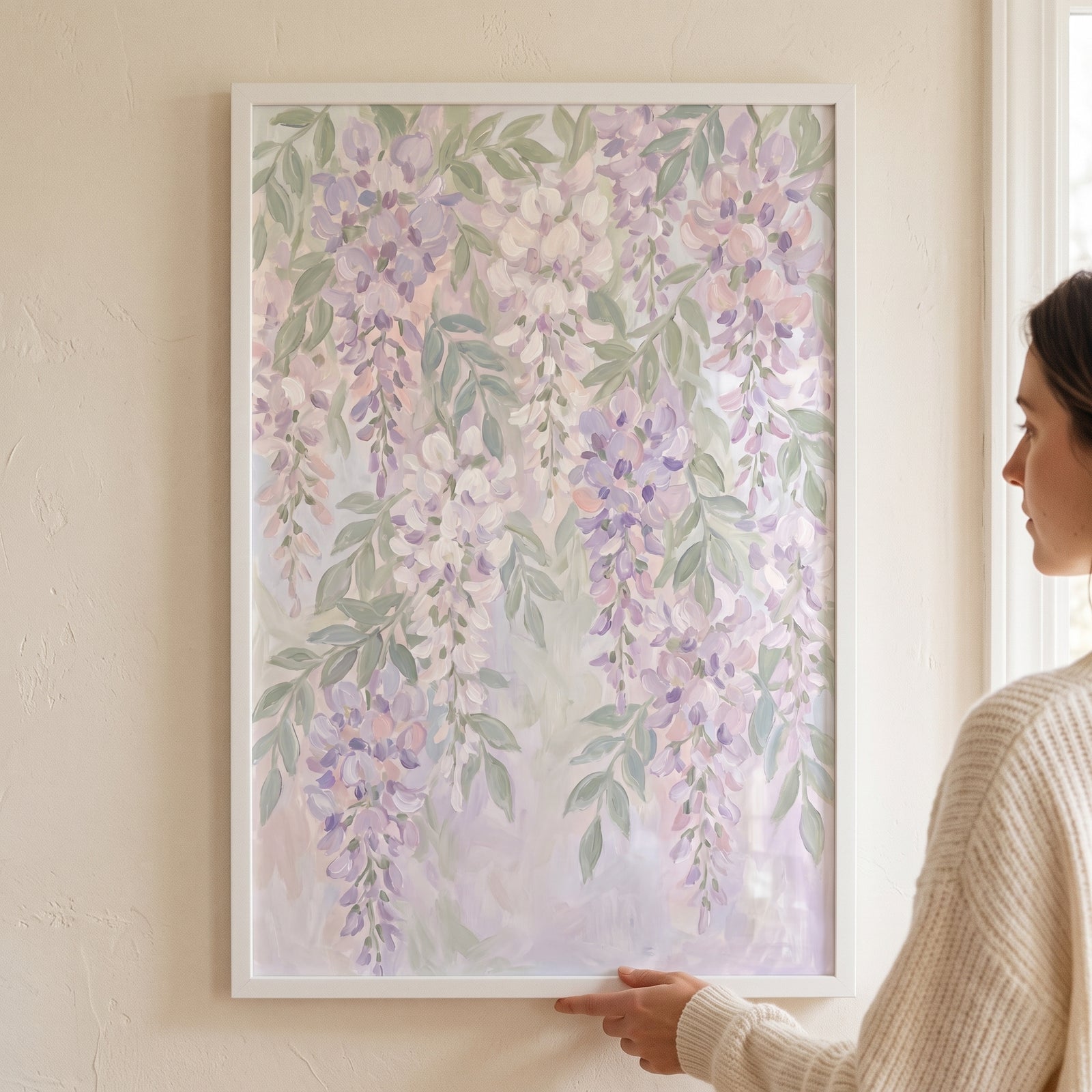 A woman holds a framed soft lavender cascading wisteria floral wall art piece against a neutral wall.