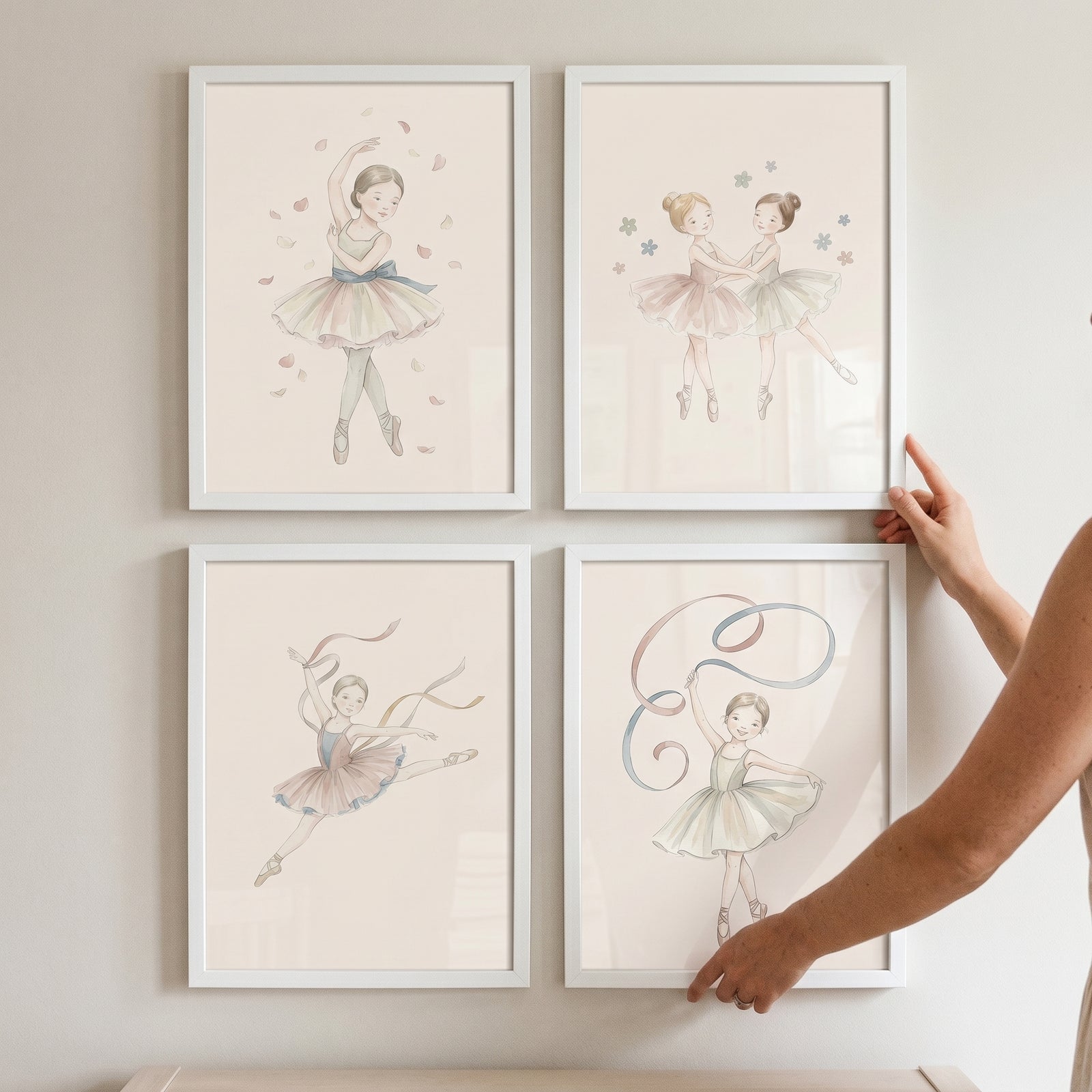 Hands adjust a soft neutral watercolor ballerina wall art set of 4 in white frames on a neutral wall.