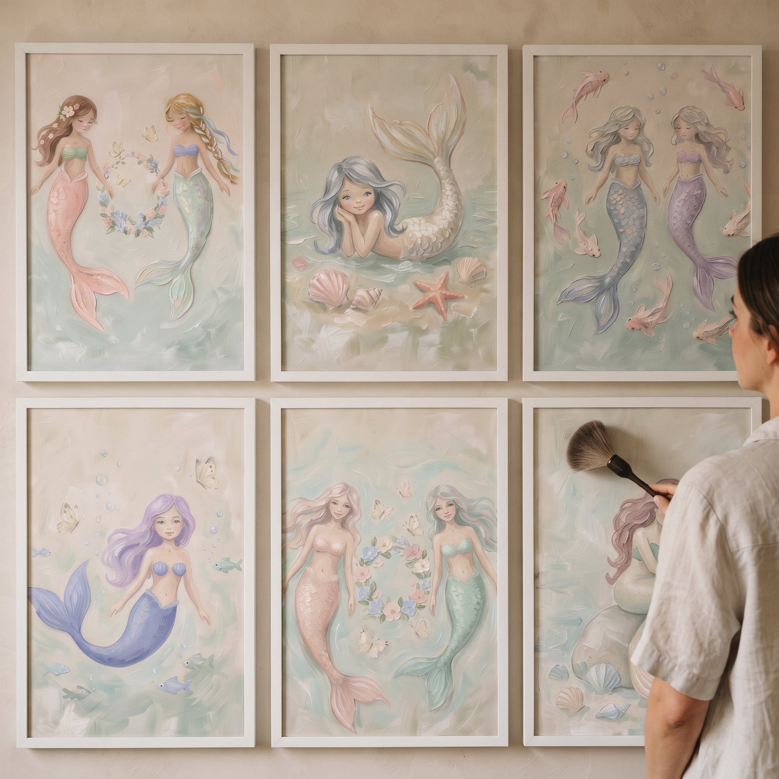 An artist touches up a soft palette mermaid wall art set of 6 with whimsical pastel illustrations in white frames.