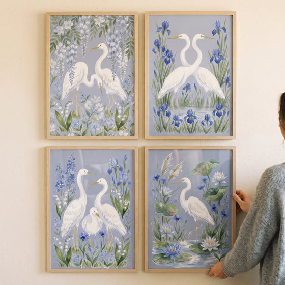 Soft pastel blue egret bird wall art set of 4 featuring white birds and flowers in wood frames on a plain wall.