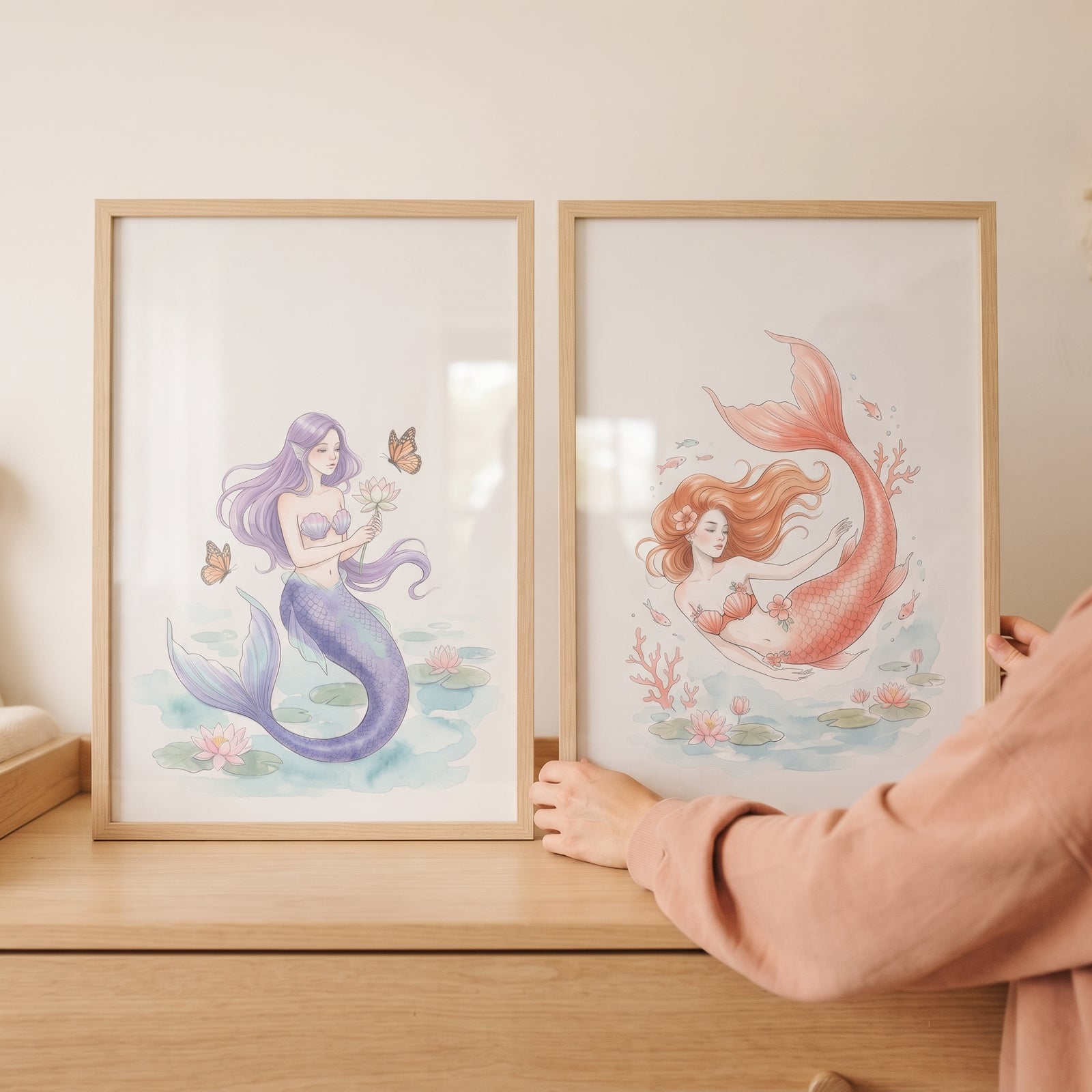 Soft pastel botanical mermaid wall art set of 2 in light wood frames being adjusted on a wooden dresser.