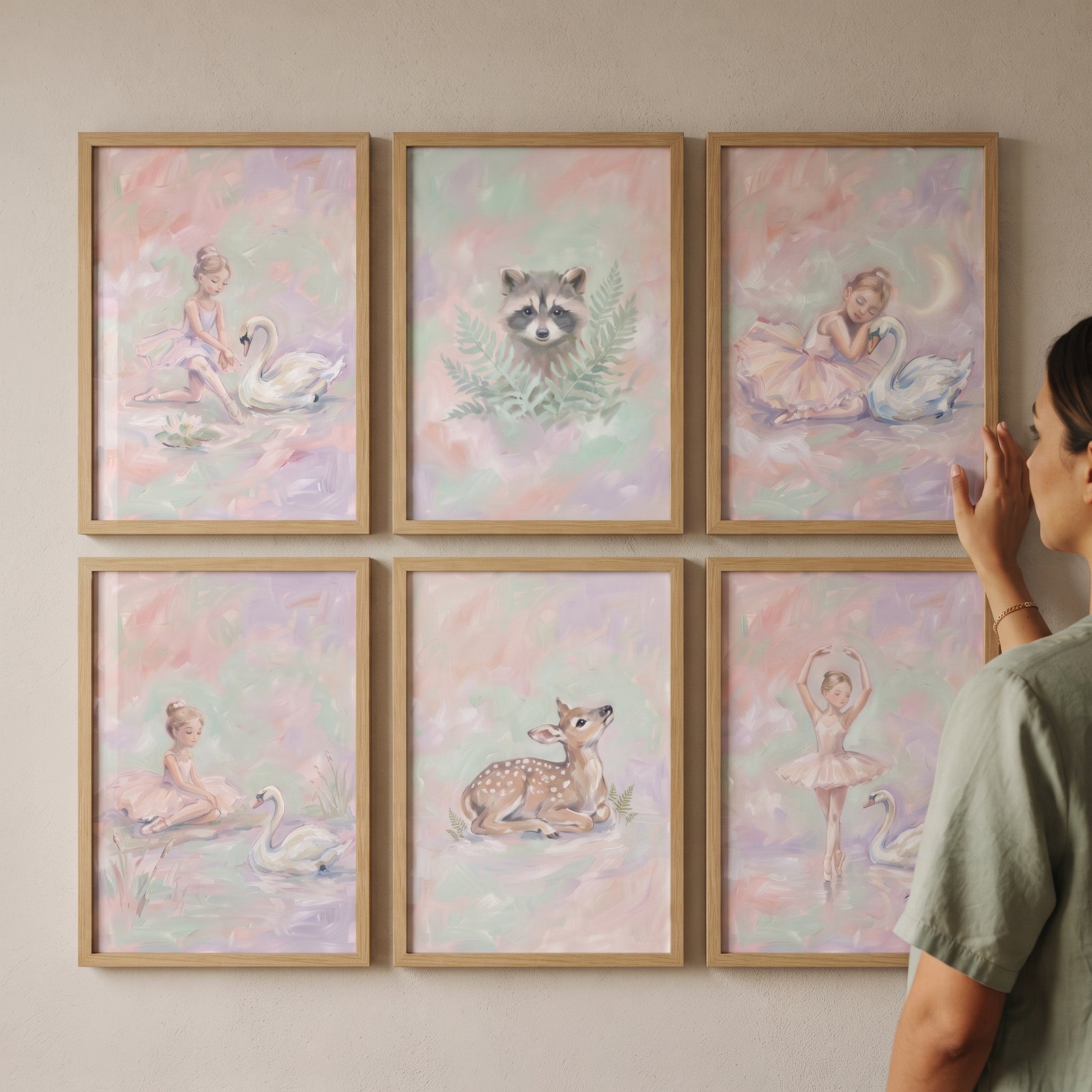 Woman arranging a soft pastel fairytale friends wall art set of 6 featuring ballerinas, swans, a raccoon, and a deer.