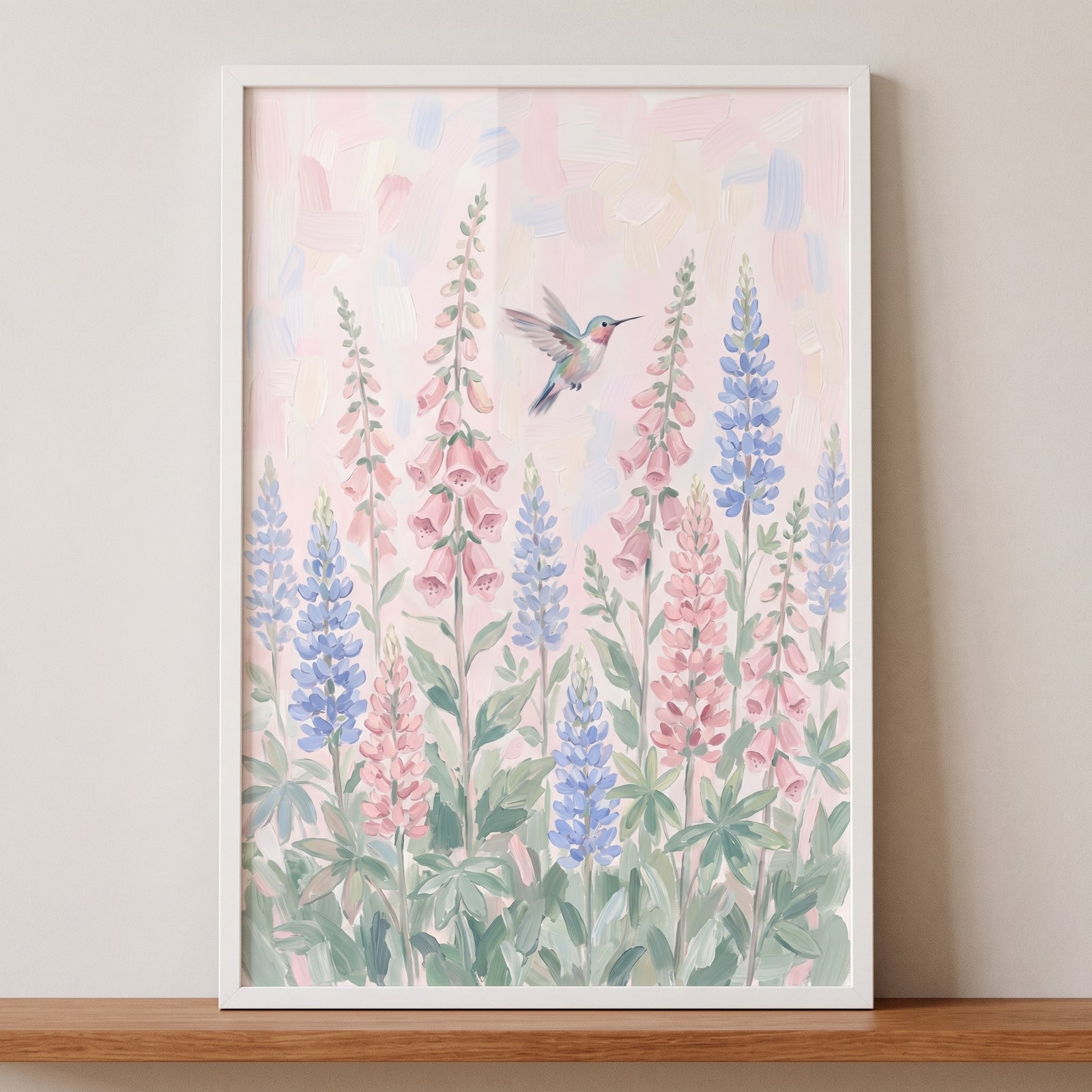 Soft pastel flying hummingbird wall art featuring pink foxgloves and blue lupine flowers in a white frame.