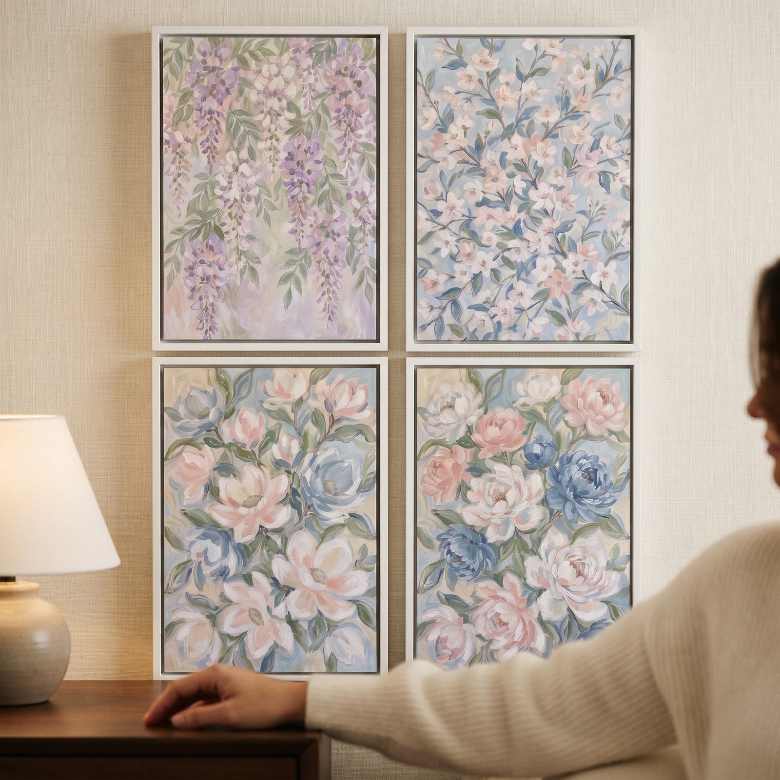 A soft pastel garden floral wall art set of 4 hangs in a grid on a wall beside a lamp and a seated person.