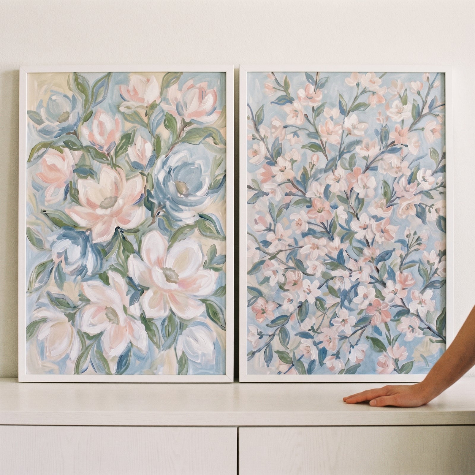 Soft pastel impressionist floral wall art set of 2 with pink and blue blossoms in white frames resting on a ledge.