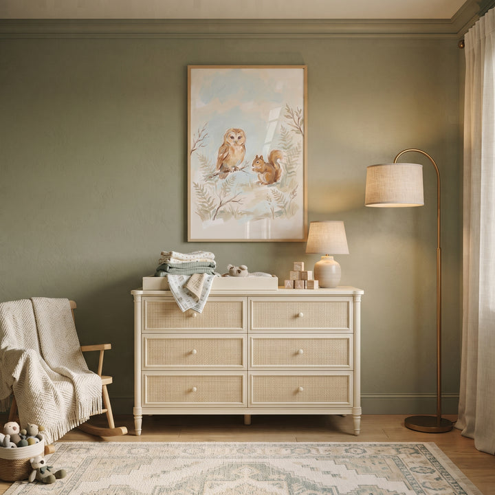 Soft pastel owl squirrel animals wall art hangs above a cream dresser in a sage green nursery with a rocking chair.
