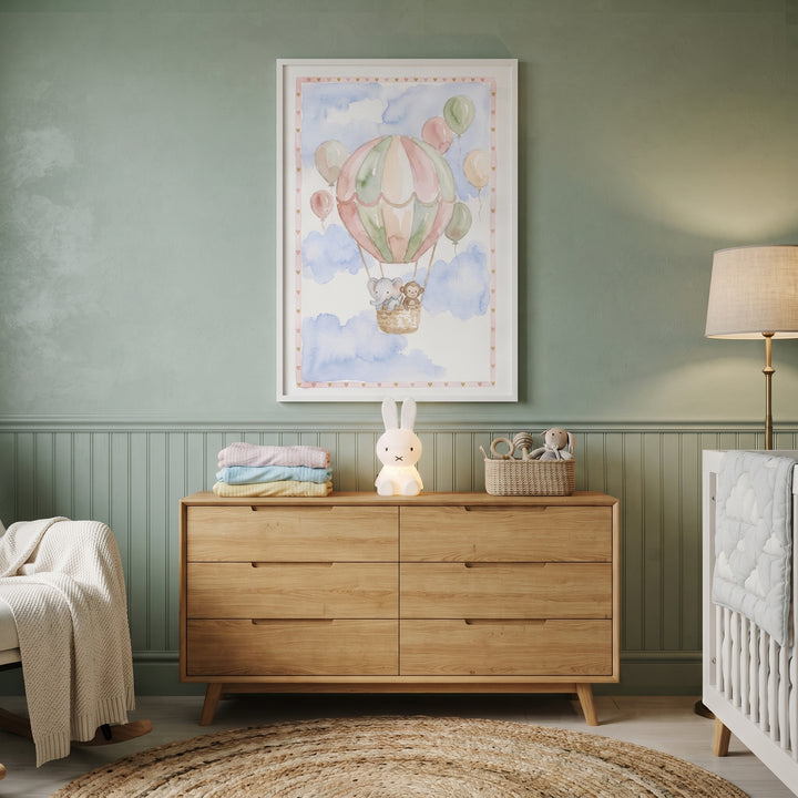 A sage green nursery features soft pastel safari animal wall art above a wooden dresser and a rabbit-shaped lamp.