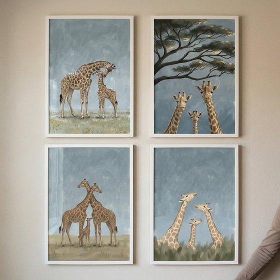 Four framed giraffe paintings arranged in a grid show gentle family moments in soft blue and neutral tones. The artworks include adult giraffes nuzzling a calf, three giraffes looking forward beneath a tree, two adults standing protectively beside a baby giraffe, and a small giraffe between two adults rising above tall grass.