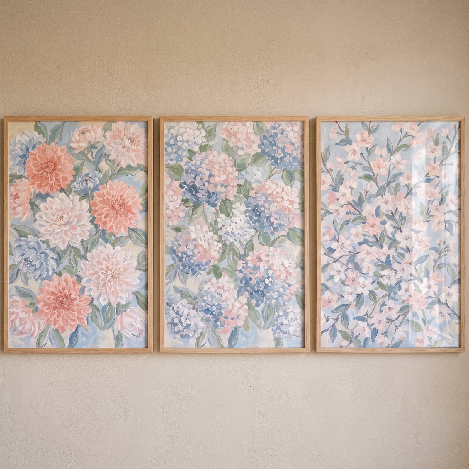 Soft pastel spring floral wall art set of 3 in light wood frames featuring pink and blue blooms on a neutral wall.
