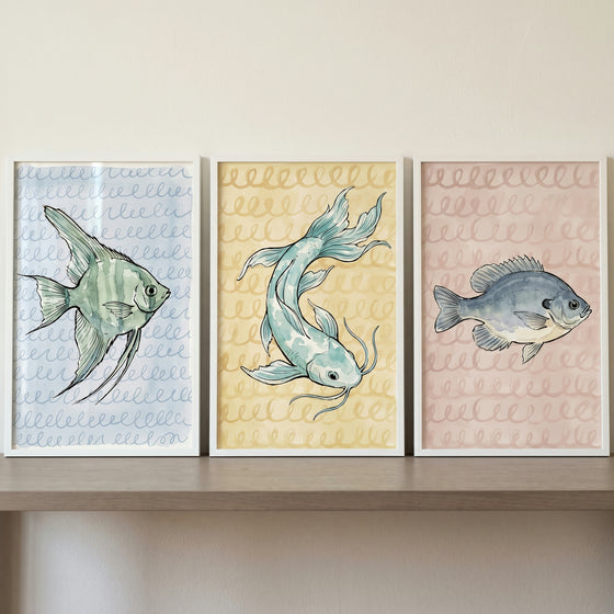 Soft pastel watercolor fish wall art set of 3 in frames on a shelf, with blue, yellow, and pink patterned backgrounds.