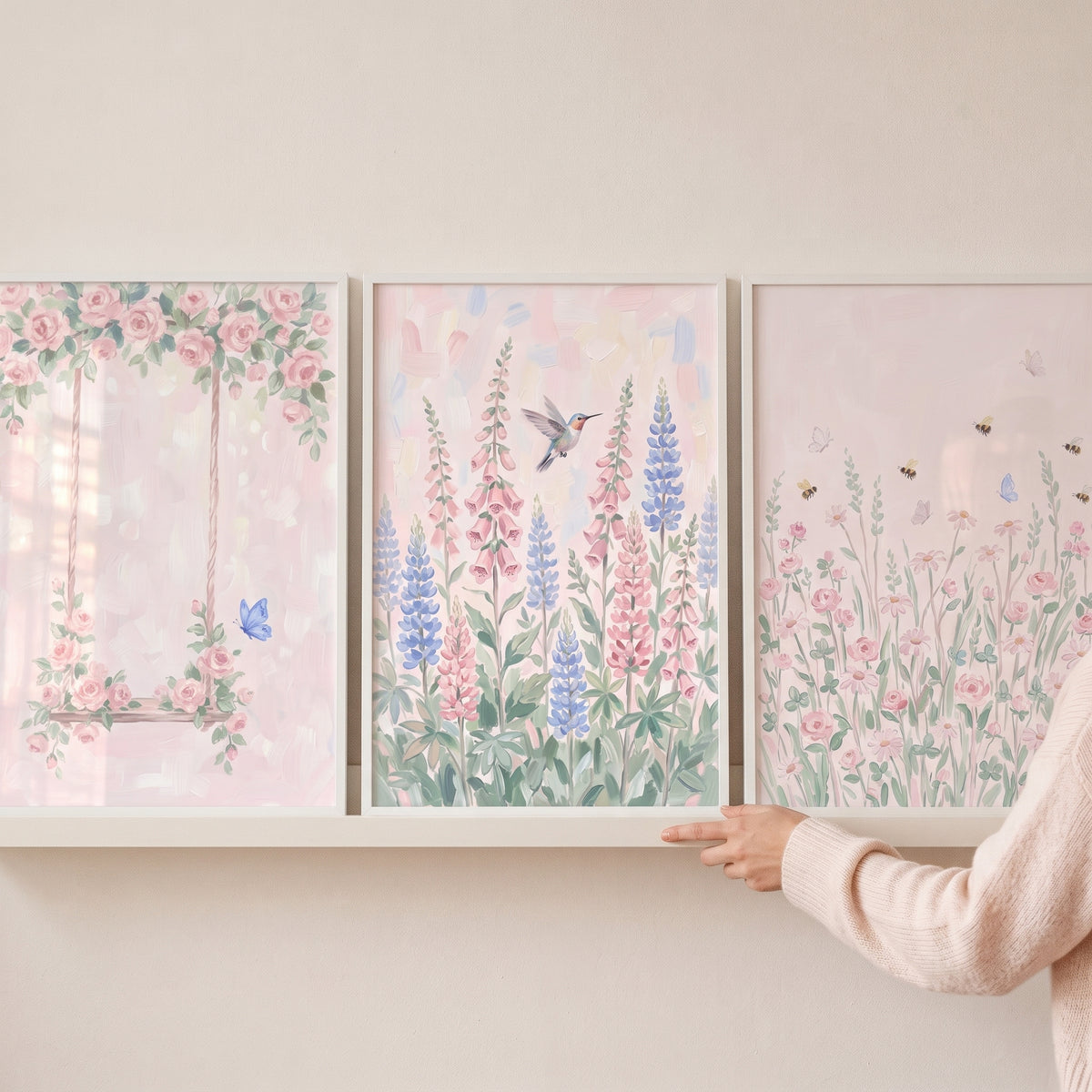 Hand adjusts a soft pink botanical garden wall art set of 3 featuring a floral swing, hummingbird, and bees.