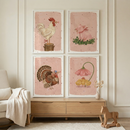 Four framed illustrations are arranged in a square grid on a light-colored wall above a wooden dresser. Each piece features a different farm animal against a soft pink backdrop with subtle dots. The top left shows a white rooster on a stump, while the top right depicts a pink pig with a red bow. The bottom left features a turkey with spread tail feathers, and the bottom right shows three yellow chicks sheltered by a large pink flower. A cream chair and a wooden toy horse add to the room.