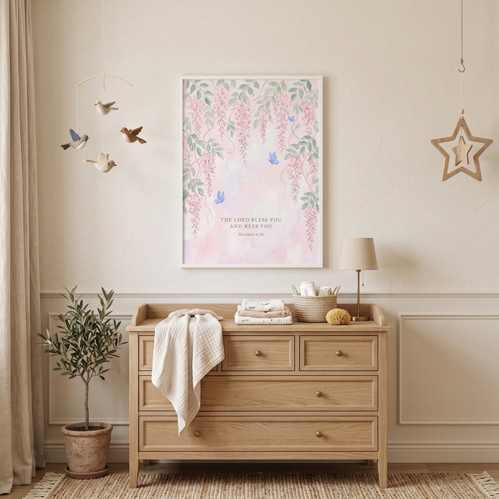 Soft pink hanging wisteria bible wall art hangs above a wooden dresser in a neutral nursery with an olive tree plant.