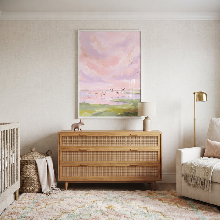 Nursery with a wooden dresser and soft pink sky flamingo bird wall art. A crib and armchair frame the neutral space.