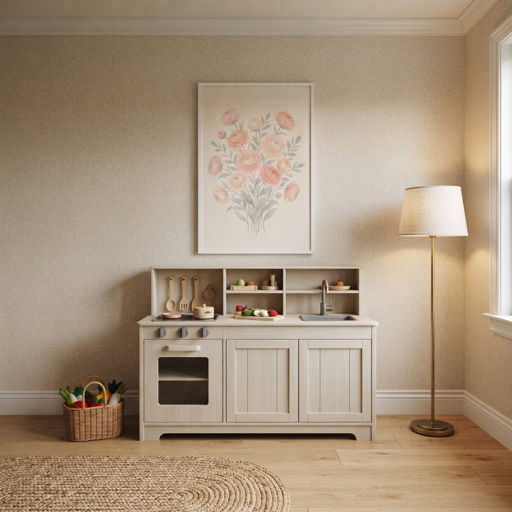 A wooden play kitchen sits below soft pink watercolor floral wall art. A lamp and woven rug accent the neutral room.