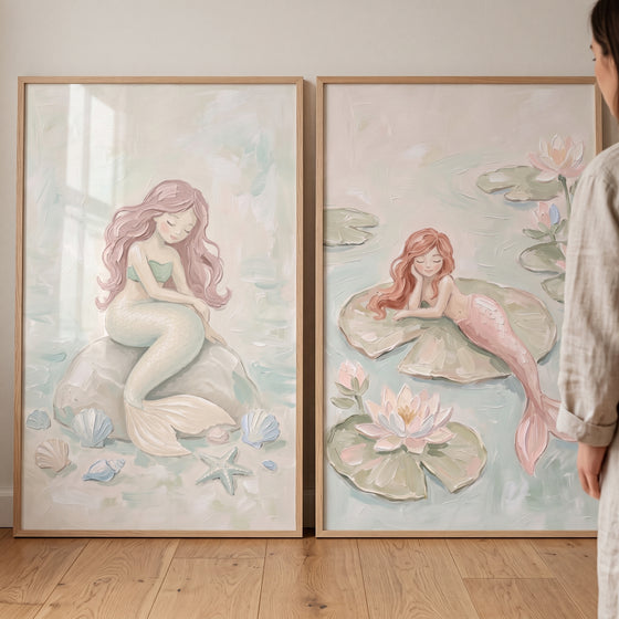 Soft pink whimsical mermaid wall art set of 2 framed prints of pastel mermaids leaning against a wall.