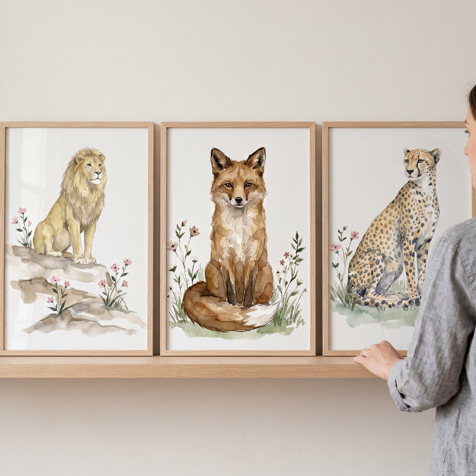 Soft pink wildflower animal wall art set of 3 featuring a watercolor lion, fox, and cheetah in wood frames on a shelf.