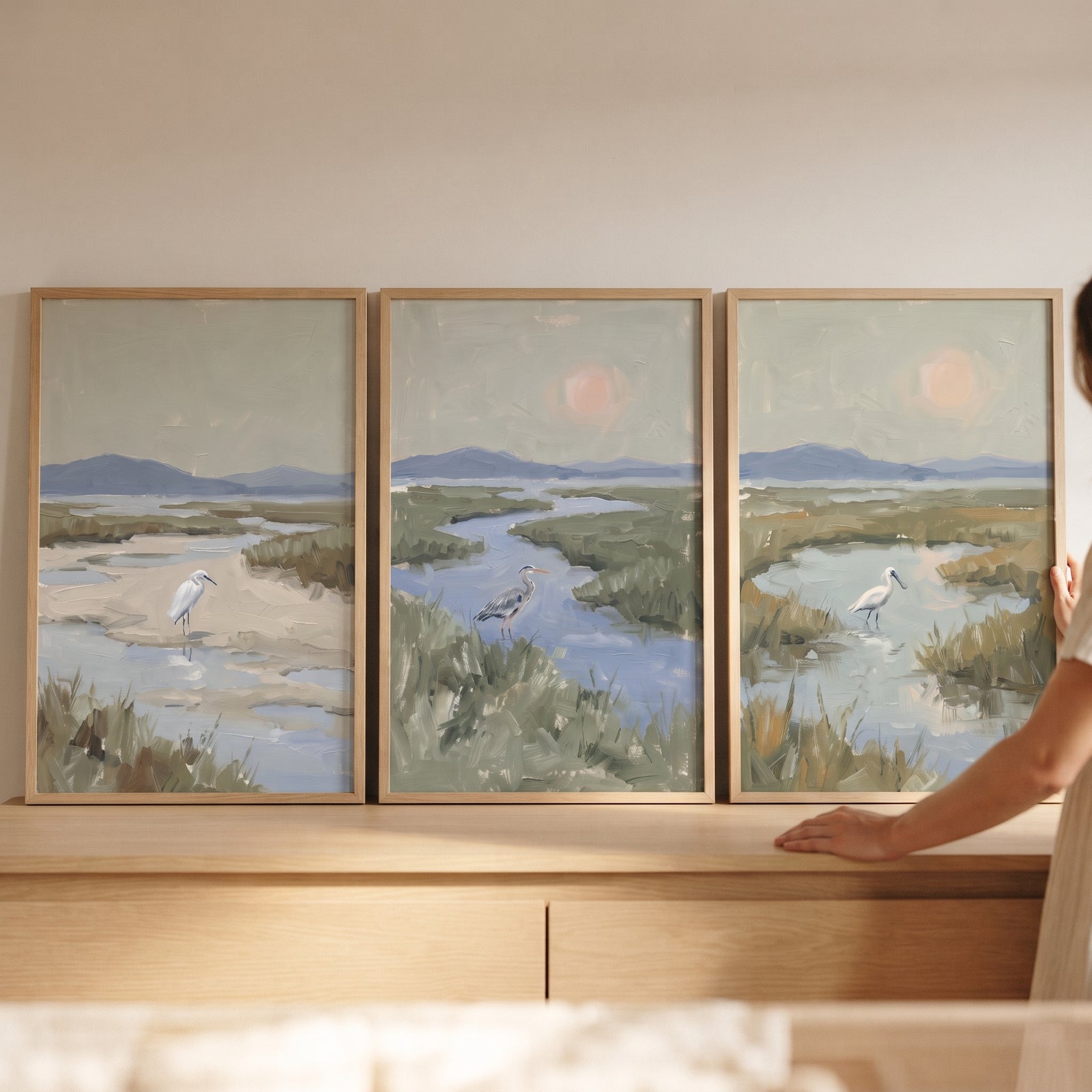 Soft sage marsh bird wall art set of 3 rests on a wood cabinet, featuring herons in a hazy, muted wetland scene.